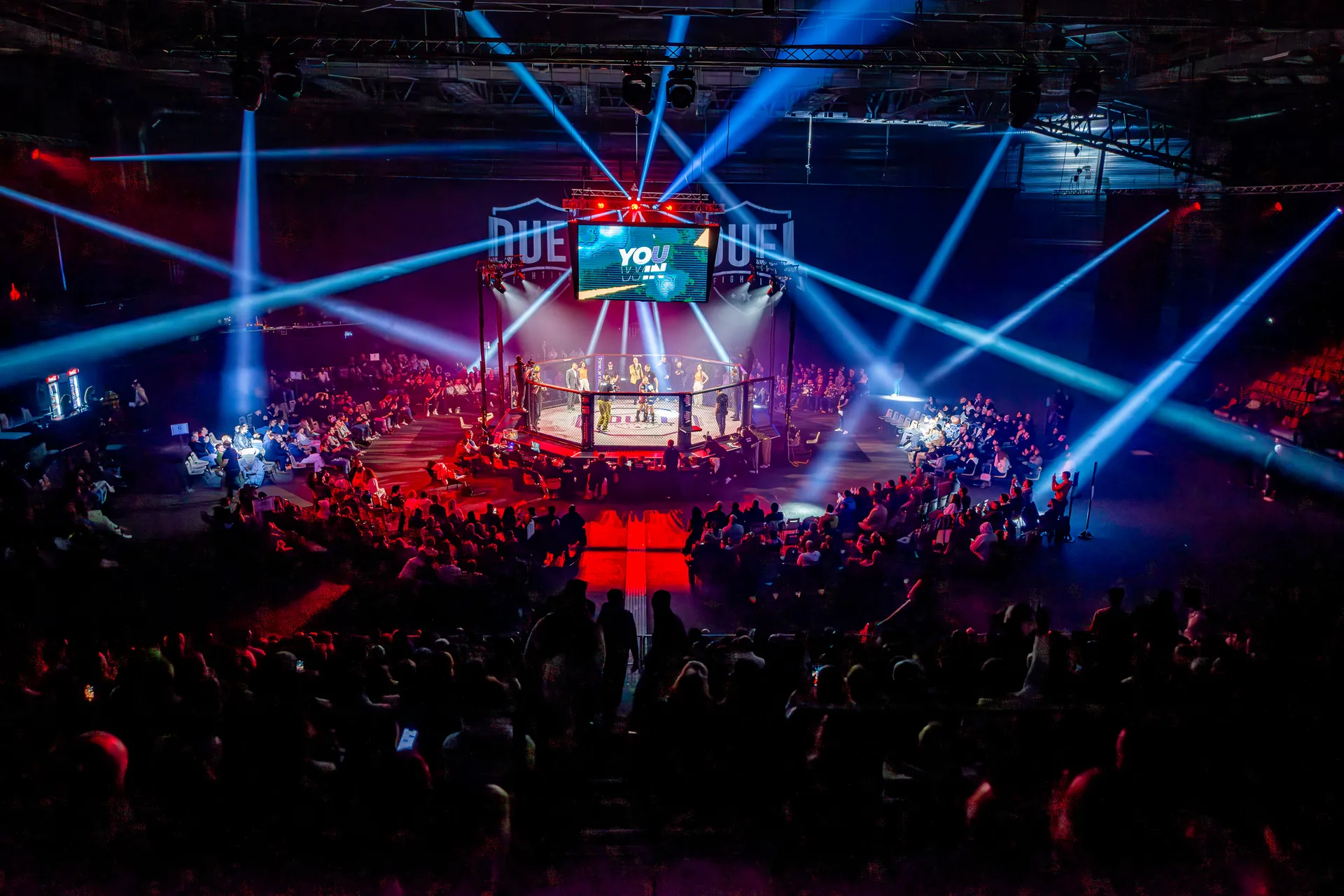 Vue d'ensemble d'une soirée Duel Fighting : cage au centre, jeux de lumière et salle comble